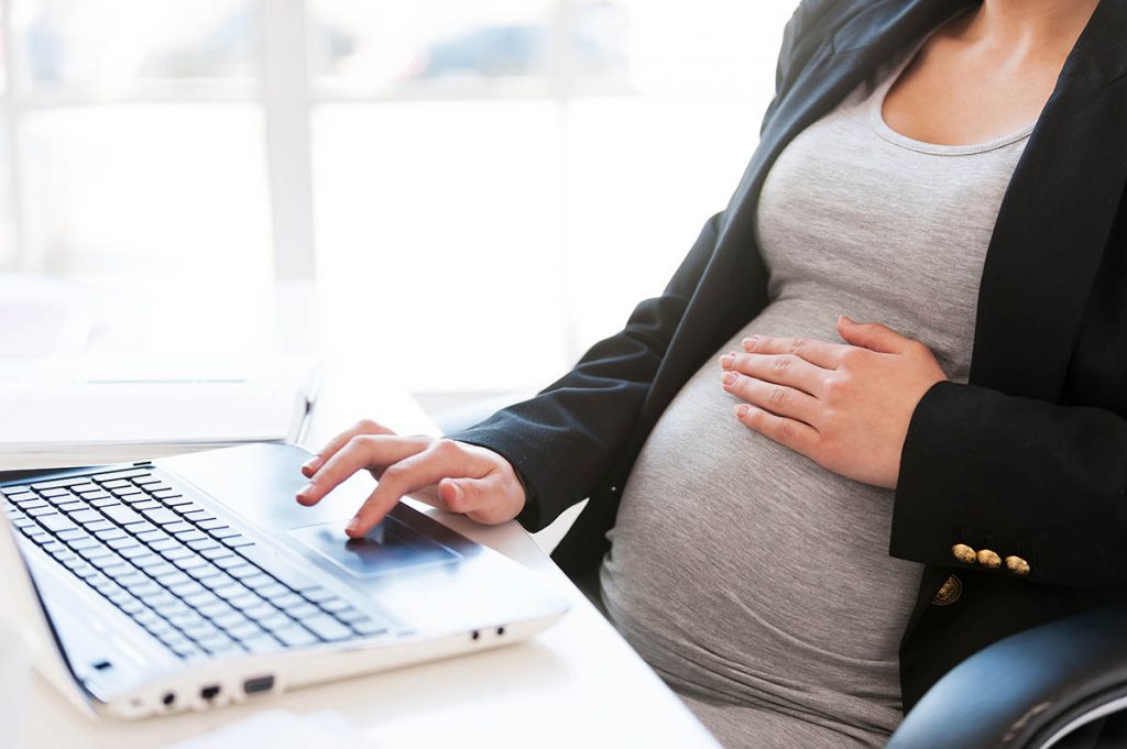 Pregnant woman on laptop looking at postpartum self-care plans
